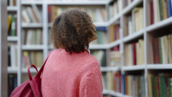 College Student Walking Among Bookcases in Library