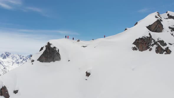 Aerial View. A Group of Skiers and Snowboarders, High in the Mountains, Prepare for a Steep Descent