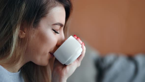 Face of Attractive Beauty Girl Drinking Hot Beverage Smiling Holding Mug Relaxing at Home Closeup