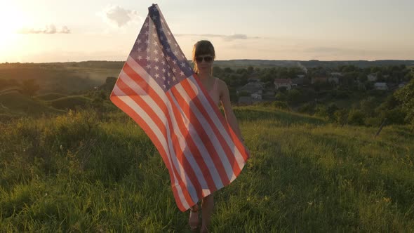 Happy young woman posing with USA national flag standing outdoors at sunset. Positive girl 