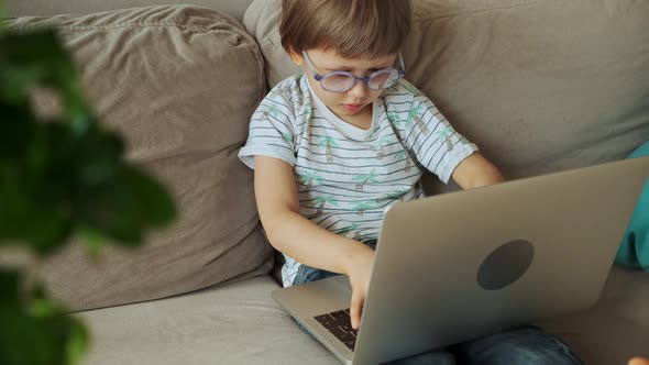 Child Playing Online Games and Using Laptop Sitting on Sofa at Home