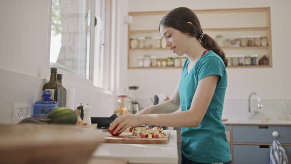 Teenage girl working cutting fruit for breakfast in the kitchen