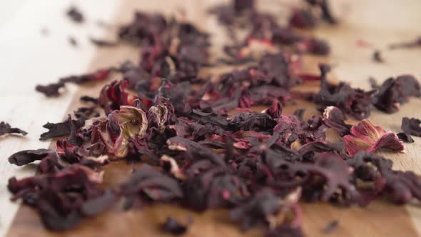 Dry natural hibiscus flower tea falls on a wooden surface