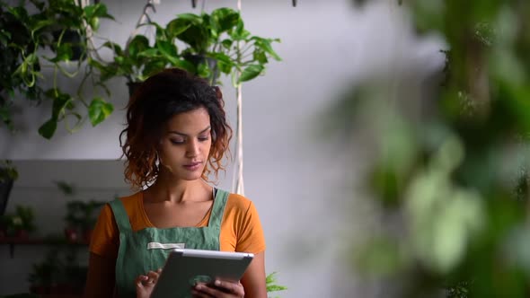 Woman Gardener Uses Tablet and Works with Plant While Standing in Light Interior Spbd
