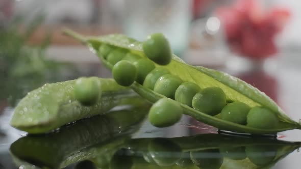 Green Peas Falling Into Table Beside Its Open Pod. - close up, slow motion