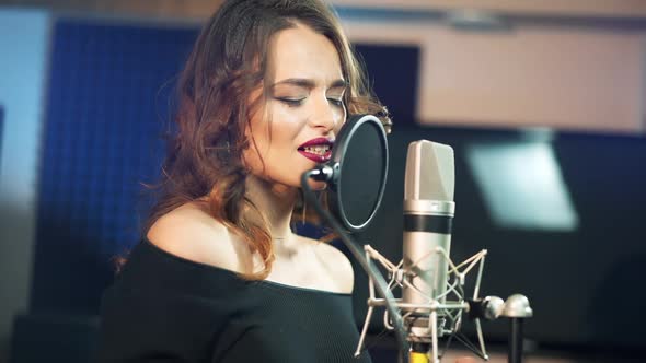 Young brunette woman recording a song or album in a professional studio.