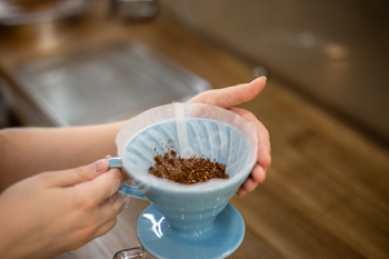 Filter with ground coffee in funnel in focus. Drip filter coffee brewing.