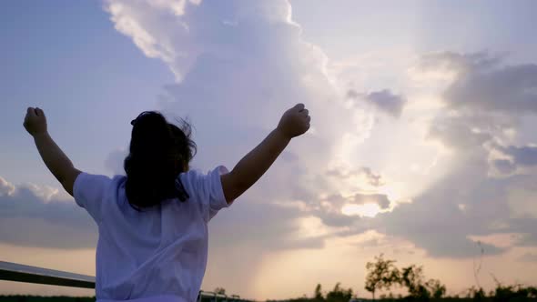 Back view of Asian girl jumping on the ground at farm, watching beautiful sunset