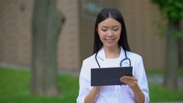 Smiling Female Doctor Working on Tablet PC in Hospital Park