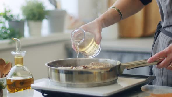 Woman pouring white wine to stewing meat in frying pan