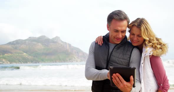 Couple using digital tablet on beach