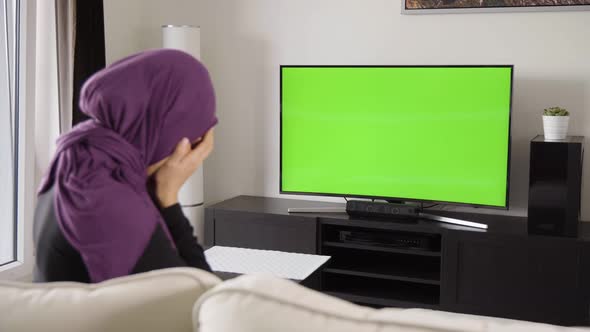 A Muslim Woman Cries and is Unhappy As She Watches TV with Green Screen in an Apartment