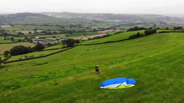 Parallax view of a paraglider inflating his wing before take off with beautiful English countryside