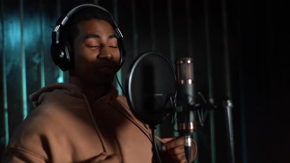 Closeup of Young AfricanAmerican Male Singer Wearing Headphones Performing and Recording New Song