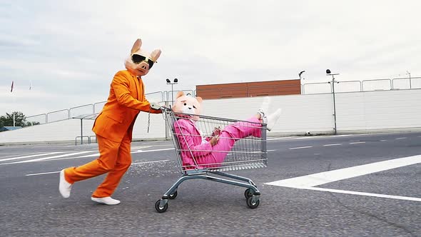 Pig man pushing bear woman in shopping cart, throwing confetti