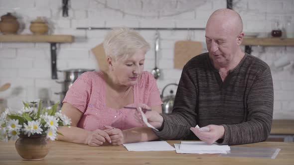 Portrait of Elderly Caucasian Couple Dealing with Bills. Bald Man and Blond Woman