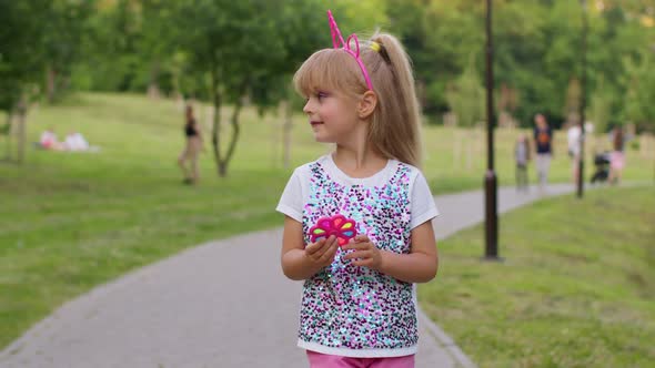 Girl Playing with Pop It Sensory Antistress Hand Spinner Squishy Bubbles Toy While Walking in Park