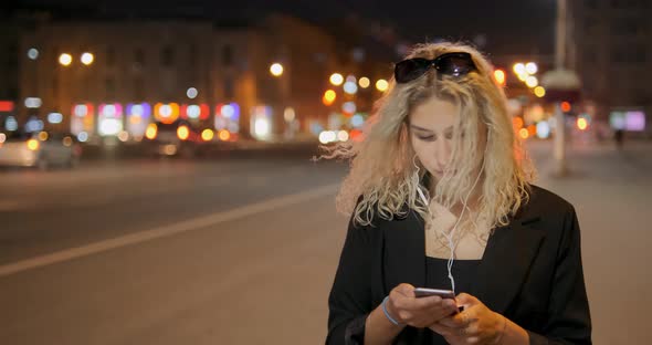 Blonde Lady in Headphones Holds Smartphone and Dances