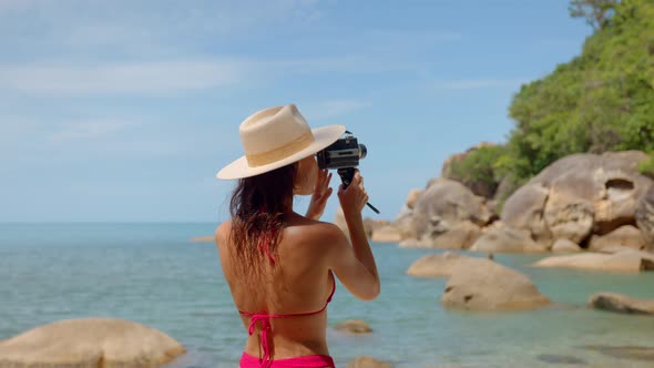 Young Traveler Woman Films Nature on Camera Dressed in Red Swimsuit and a Hat Outdoors Summertime