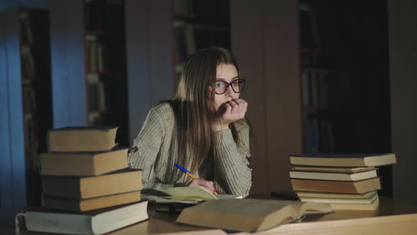 Girl Noting Compendium From Books at a Desk and Gazing Into It in Halflight