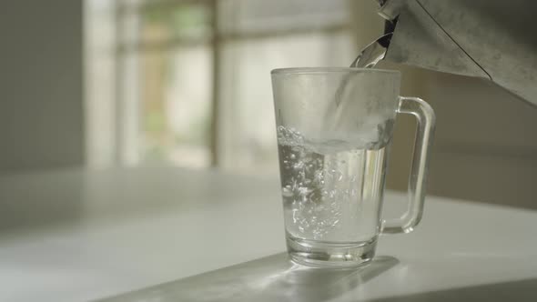 Pouring hot water from a kettle to glass mug at home