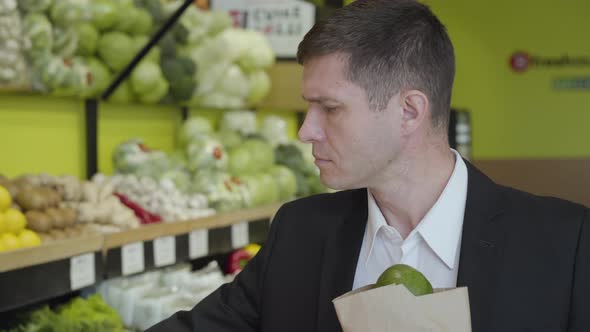 Close-up of Confident Adult Caucasian Man Choosing Pomelo in Grocery, Putting Citrus Fruits Into