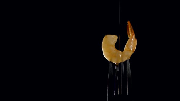 freshly cooked juicy shrimp on a fork is poured with olive oil on a black background. healthy food 