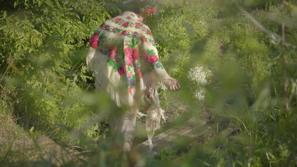 Beautiful Overweight Woman with a Wreath on Her Head and Flowers in Hands Going Through the Small