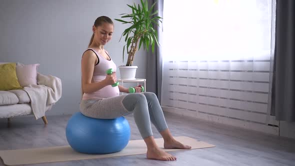 Pregnant Woman Sit on Fit Ball Working Out with Dumbbells in Home Living Room Spbd