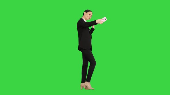 Smiling Businesswoman Taking Selfie on Her Phone While Walking on a Green Screen, Chroma Key.