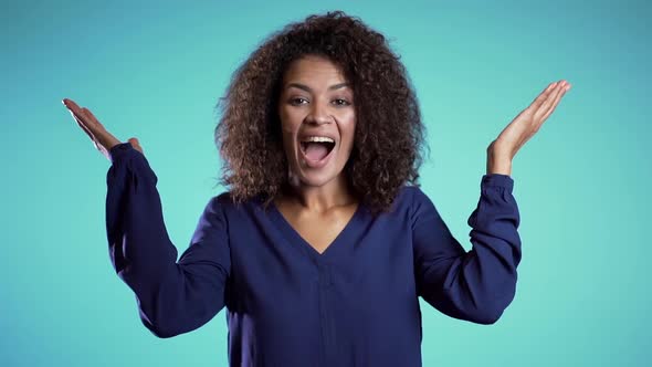 woman with afro hair smiling, pleasantly surprised to camera over blue background.
