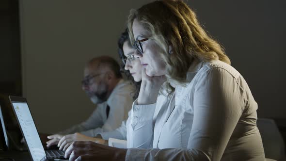 Tired Colleagues Working with Laptops in Dark Office