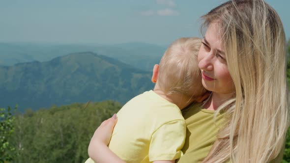 Happy Mother Strokes Little Son Against Distant Mountains