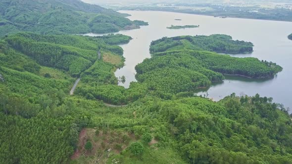 Drone Flies From Forested Highland To Large Lake