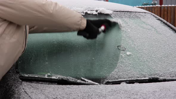 Man In Coat And Gloves Cleaning Frozen Car Windshield, Scrapes Ice Off The Glass Surfac