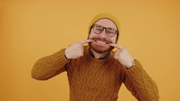 Young Handsome Caucasian Man Touches Edges of His Mouth and Shows Teeth Yellow Background Isolated