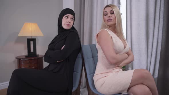 Two Women Sitting Back To Back and Looking at Each Other. Muslim and Caucasian Ladies Depicting