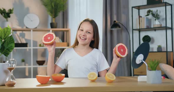 Girl Sitting in front of Camera at Home and Playing with Halfs of Grapefruit