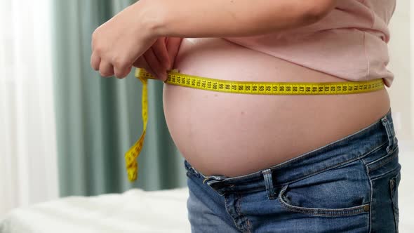 Closeup of Pregnant Woman Waiting for Baby Measuring Her Abdomen with Yellow Measuring Tape