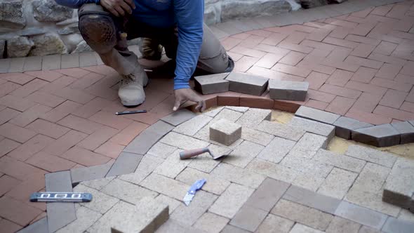 Circular steadicam shot of brick paver artisan fitting bricks into a two-tone design for a patio.