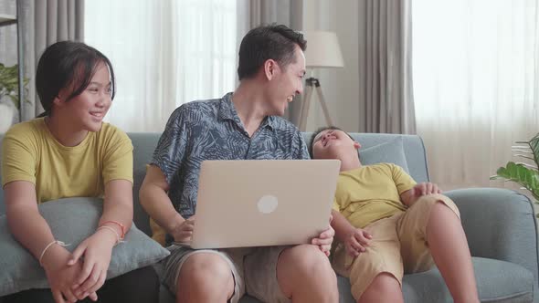 Happy Father With Two Little Children Using Laptop Together, Sitting On Sofa At Home