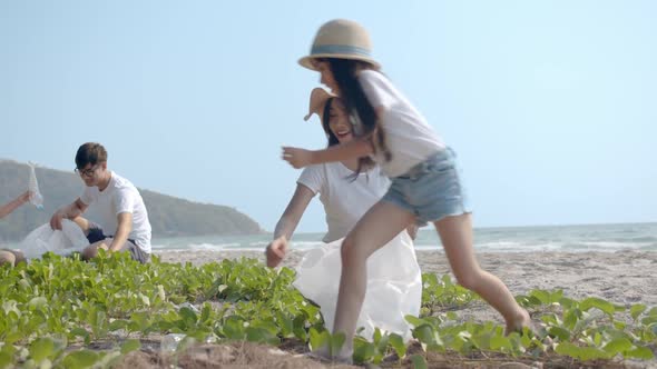 Asian family picking up plastic bottle to trash bag on the outdoor beach.