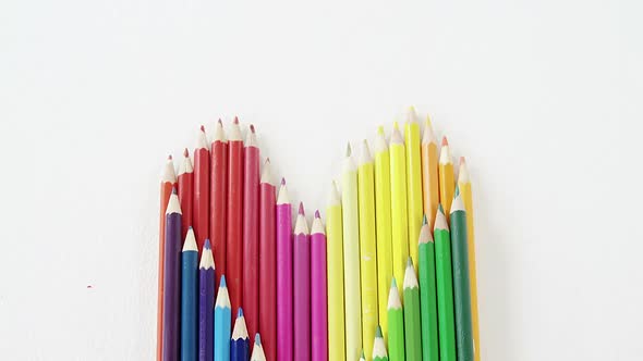 Colored pencils arranged in heart shape on white background