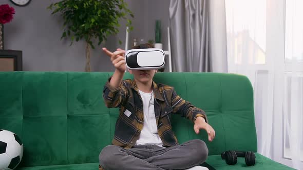 Modern Teen Boy Sitting on Soft Green couch and Using Special Futuristic 3d Glasses to Play