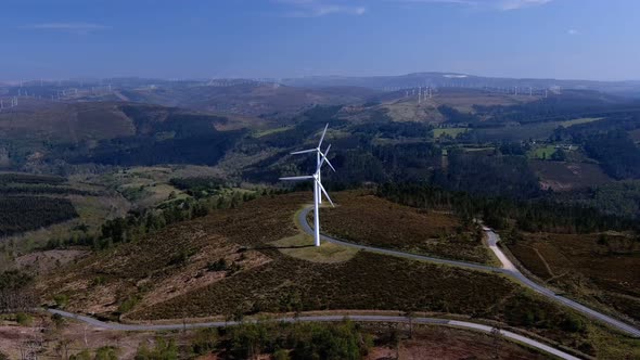 Spinning wind turbines lined up on a hill with forests connected by roads, plus wind turbines in the