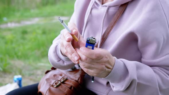 Woman Holding a Cigarette and a Lighter in Hands While Sitting in Nature on Sun