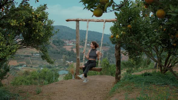 Woman Swinging Happily on Swing Beneath Tree in the Orange Garden in Slow Motion