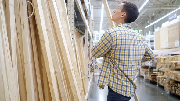 Young Man Chooses Wooden Beams in a Building Materials Store