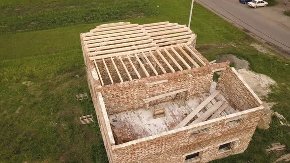 Aerial view of a brick house with wooden ceiling frame under construction.