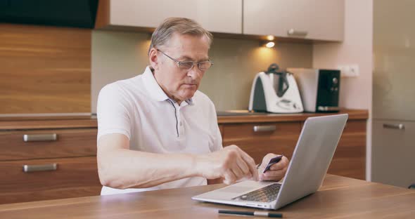 Warm Toned Portrait of Modern Senior Man Shopping Online or Paying Taxes Holding Credit Card While